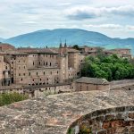 A Urbino il teatro si fa letteralmente in quattro: il festival URBINO TEATRO URBANO dal 10 al 17 luglio, la rassegna teatrale UTU PIAZZE nei comuni della Valle del Metauro e del Montefeltro fino alla fine di Agosto, il protocollo GODOT (unico in Italia) pensato ad hoc per gestire gli eventi dal vivo sotto pandemia e il corso di alta formazione per operatori teatrali FAI IL TUO TEATRO con i più importanti professionisti del settore (dal 10 al 17 luglio a Urbino).   In un’estate in cui molti eventi dal vivo sono stati annullati o drasticamente ridimensionati URBINO TEATRO URBANO sceglie la resilienza e punta tutto sulla cultura e sul teatro come elemento di aggregazione e di ricostruzione di una comunità ferita dal Covid. Sceglie anche di fare rete con il mondo dei lavoratori dello spettacolo offrendo gratuitamente GoDot, un protocollo integrato di segnaletica e strumenti digitali anti covid e un corso, sempre gratuito, per fornire agli operatori gli strumenti concreti per gestire la proprio attività.   “In tutte le proposte del festival, dalla formazione agli spettacoli dal vivo, vogliamo invitare il pubblico a reinterpretare lo spazio del vivere comune – ha dichiarato Michele Pagliaroni, Direttore artistico di Urbino Teatro Urbano -  Se siamo riusciti ad organizzare questa terza edizione è soprattutto grazie all'aiuto dagli studenti (uno staff di circa 40 giovani), per i quali Urbino Teatro Urbano costituisce un'occasione per ritrovarsi in sicurezza, ripensare la città insieme ai suoi cittadini e arricchire la propria esperienza universitaria, anche grazie alla preziosa collaborazione di ERDIS. Il progetto è il frutto di un dialogo reale, tangibile fra l'Università, la città e il territorio. Abbiamo deciso di dedicare la prima serata ad uno spettacolo che parla di luna e conquiste spaziali: come i marinai persi nella tempesta ci affidiamo alle stelle per ritrovare la rotta del nostro cammino.  ”   UTU (10, 11, 12 e 17 luglio, Urbino, Urbania e Isola del Piano) Il programma del Festival, che ha come suo centro propulsore Urbino, si snoda in quattro appuntamenti, tutti diversi nei temi e nei linguaggi scenici, allestiti in quattro diversi spazi: una scelta dettata dalla volontà di mettere al centro il pubblico nella sua varietà e condurre lo spettatore a riveder le stelle dopo l’Inferno della quarantena. Ecco quindi che la scienza, il teatro e Urbino stessa diventano protagonisti della scena in una narrazione sempre diversa, dimostrando che quello del teatro è davvero un linguaggio universal, capace di parlare a tutti e di abitare spazi e funzioni sempre diverse ma sempre significative.   La terza edizione del Festival URBINO TEATRO URBANO riparte proprio dalle stelle il 10 luglio con ROCK AROUND THE MOON, la conferenza-concerto del planetologo Ettore Perozzi che ci porta sulla luna in compagnia delle più belle canzoni dedicate agli astri cantate da Raffaella Misiti con l’accompagnamento di Annalisa Baldi. Il programma prosegue l’11 luglio con URBINO PRIMO CITTADINO, performance itinerante a cura del CTU Cesare Questa, uno spettacolo allestito specificamente per il festival con la drammaturgia originale di Aureliano Delisi che firma anche la regia insieme a Michele Pagliaroni. Gli ultimi due appuntamento sono dedicati al mondo del teatro: in anteprima nazionale il 12 luglio il nuovo lavoro di Paolo Mazzarelli SOFFIAVENTO nel cortile del Palazzo Ducale di Urbania, mentre l’ultimo appuntamento del Festival è in programma il 17 luglio a Isola del Piano con PAROLE IMBROGLIATE omaggio ad Eduardo di e con Massimiliano Civica.   UTU #PIAZZE (luglio e agosto, vari comuni della provincia di Pesaro e Urbino) Quest’anno il progetto UTU, in accordo con la città, con l’Università, con le Unioni Montane e con AMAT, supera le mura di Urbino per un festival diffuso che animerà i comuni dell’Alta Valle del Metauro e del Montefeltro fino alla fine di Agosto. Una scelta coraggiosa per rispondere alle esigenze delle piccole comunità del territorio, che hanno aderito con entusiasmo all’iniziativa, un modo per portare la cultura nelle aree interne, nella convizione che grazie alla partecipazione dei cittadini è possibile valorizzare le risorse del territorio e sostenere le comunità.   GoDot (prima sperimentazione 10-17 luglio Urbino) UTU è il primo festival che ha ideato e sviluppato un protocollo anti contagio pensato ad hoc per lo spettacolo dal vivo. Divertente, colorato, flessibile e sostenibile, il protocollo GoDot permette di gestire I flussi di pubblico grazie alla creatività, trasformando il distanziamento in un’opportunità poetica e in un gioco a partire già dal nome composto da Go (vai) e Dot (punto, stai fermo). Grazie alla segnaletica specifica disegnata da ISIA, il pubblico viene guidato nell’evento sin dalla fila al botteghino, riceve tutte le informazioni necessarie e partecipa allo stesso tempo a un divertente percorso interattivo. Inoltre, grazie alla app WOM DiAry - sviluppata da Digit srl, nata nell’Università di Urbino -  è possibile effettuare il tracciamento senza la condivisione di dati personali, accedere a contenuti speciali, ottenere sconti e promozioni nei negozi del territorio. I riscontri del pubblico e del territorio vengono raccolti e monitorati da un team di docenti e studenti di Sociologia. Il protocollo GoDot è in continuo aggiornamento grazie al contributo di tante realtà che hanno chiesto di adottarlo, come Frigid New York, Pentación Espectáculos di Madrid, Deputacion Foral de Gipuzkoa (Paesi Baschi) e oltre quaranta tra festival e teatri italiani.   Fai Il tuo teatro (10-17 luglio, Urbino) Ripartire. Quante volte abbiamo sentito questo verbo, ma ripartire per lo spettacolo dal vivo è un’impresa difficile che richiede grande tenacia ma anche grande competenza. Ecco quindi che UTU ha pensato al corso gratuito di alta formazione FAI IL TUO TEATRO pensato per artisti e addetti ai lavori. In una settimana i partecipanti potranno acquisire i primi strumenti per organizzare, produrre, comunicare uno spettacolo, per coinvolgere il pubblico e scegliere i materiali di lavoro fino a progettare una locandina o addirittura realizzare autonomamente un palco in legno. I docenti del corso sono stati scelti tra i più importanti professionisti del settore: Franco Cordelli (scrittore e critico teatrale del Corriere della Sera) terrà un corso di letteratura teatrale, Mimma Gallina (docente alla Paolo Grassi di Milano) parlerà di organizzazione dello spettacolo, lo scenografo e maestro mascheraio Stefano Perocco di Meduna guiderà gli allievi per la scenotecnica, Giorgio Testa e la Casa dello Spettatore si occuperanno del lavoro sul pubblico, Gianluca Balestra presidente di Elsinor centro di produzione teatrale terrà la classe di produzione, Debora Pietrobono, esperta di comunicazione culturale e ufficio stampa di ERT, si occuperà della comunicazione, Danilo Mancini condurrà un workshop di  grafica e Francesco Mentonelli invece seguirà il corso di illuminotecnica. Sono oltre 40 le compagnie che hanno aderito all’offerta formativa per un totale di oltre 120 corsisti che seguiranno le lezioni tutti i giorni dalle 9 alle 19 in vari spazi tra il Cortile di Santa Chiara, il Cinema Teatro Ducale e il Teatro Sanzio.    UTU, #piazze e GoDot sono ideati e sviluppati dal CTU “Cesare Questa” in collaborazione e con il patrocinio di Regione Marche, Provincia di Pesaro e Urbino, Comune di Urbino e Comuni dell'Alta Valle del Metauro e del Montefeltro, Università degli Studi di Urbino Carlo Bo, AMAT, ERDIS, Club per l’UNESCO di Urbino e del Montefeltro, Legato Albani, DIGIT srl, Cinema Teatro Ducale, ISIA U, Urbino Jazz Club, Danilo "Sailor Danny" Mancini, Festa di Teatro Eco Logico di Stromboli, Casa dello Spettatore, Consorzio Marche Spettacolo, partner tecnico Urbino Incoming.